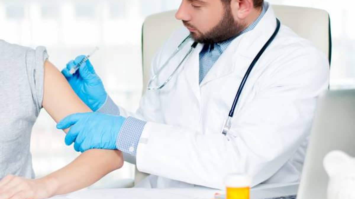 Pharmacist administering a vaccine to a seated adult patient