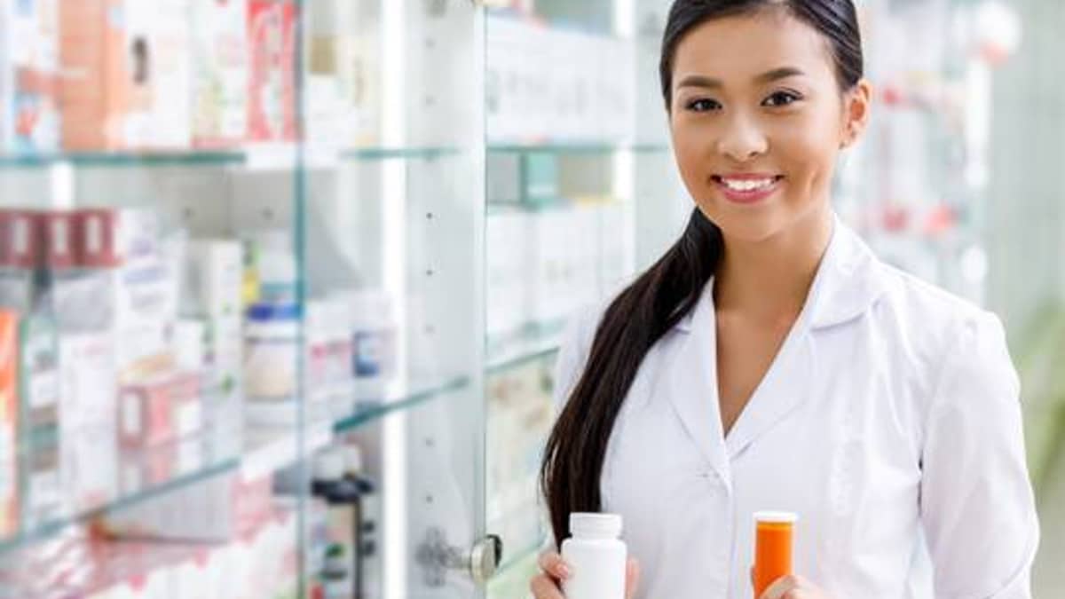 Pharmacist holding supplement bottles beside a display case of wellness products
