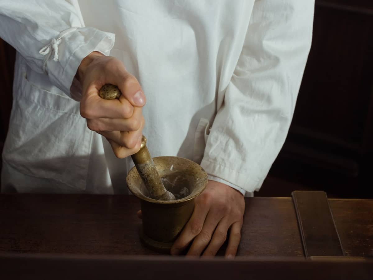 Hands grinding ingredients with a mortar and pestle on a compounding bench